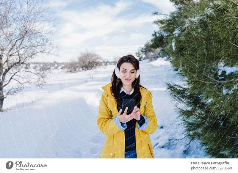 junge schöne Frau hört Musik auf Handy und Headset im Schnee. trägt gelben Mantel, Winter-Lifestyle hören Berge u. Gebirge Technik & Technologie tagsüber
