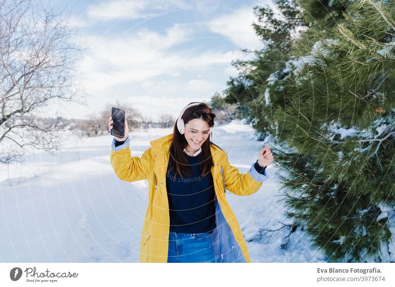 junge schöne Frau hört Musik auf Handy und Headset im Schnee. trägt gelben Mantel, Winter-Lifestyle hören Berge u. Gebirge Technik & Technologie tagsüber