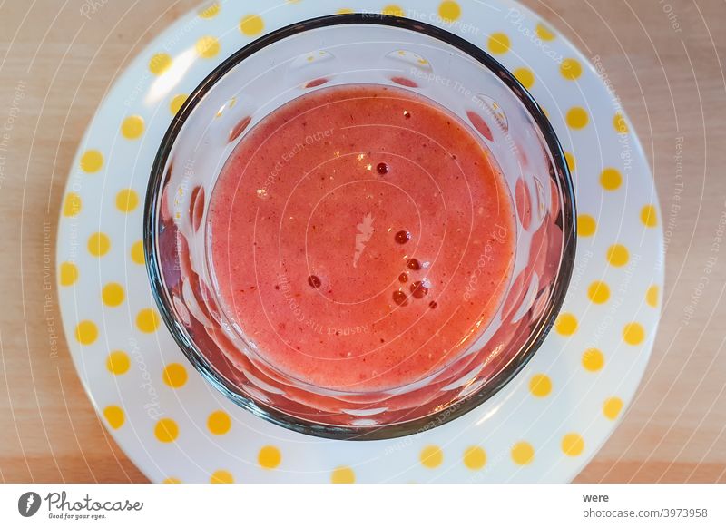 Frischer roter Fruchtsmoothie in einem Glas auf einem weißen Teller mit gelben Punkten Frischer roter Frucht-Smoothie Verteidigungen trinken Fitness frisch