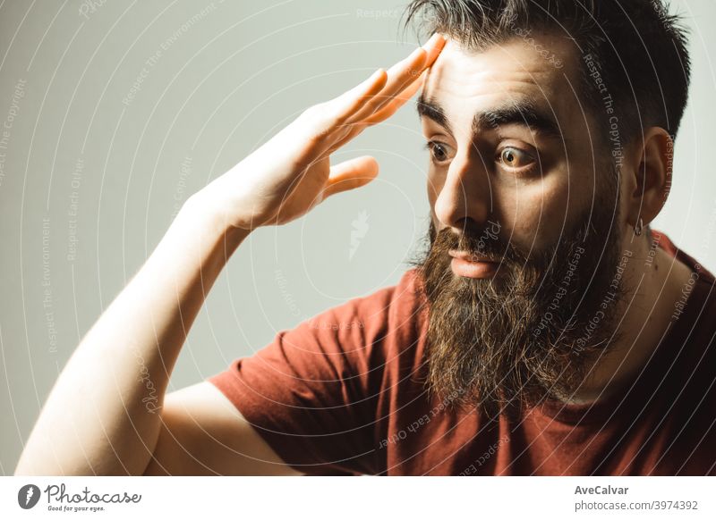 Ein junger Mann im Hipster-Stil mit Bart und modernem Haarschnitt überrascht, während er auf sein Telefon mit seinem Handy-Bildschirm mit Kopie Raum gewinnen