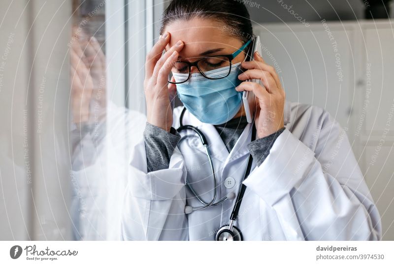 Besorgte Ärztin beim Telefonieren Arzt sprechend Mobile traurig schlechte Nachrichten pandemische Müdigkeit beunruhigt Stress verzweifelt Schutzmaske