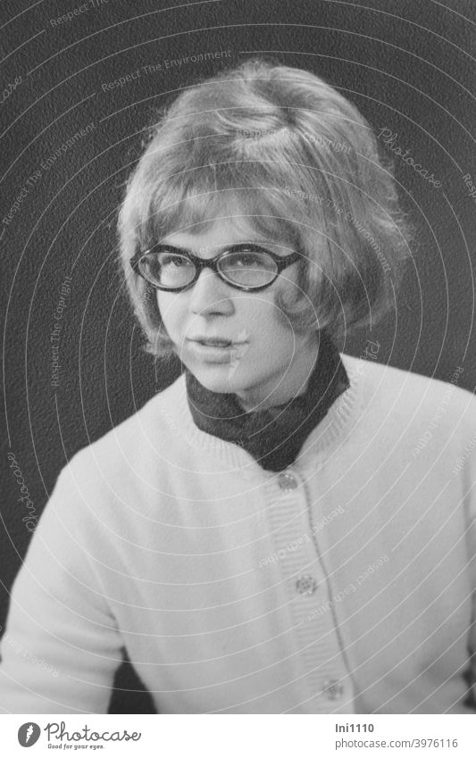 junge Frau in den 60-er Jahren mit Brille trägt Haarfrisur mit Herrenwinker Nostalgie Portrait lächelnde Frau Strickjacke Halstuch schwarz weiß Junge Frau