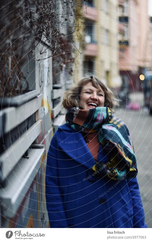 LACHEN - GLÜCKLICH - LEBEN Frau blond Locken Winter Herbst Schal Jacke blau Hauswand Freude Lebensfreude Außenaufnahme Farbfoto Fröhlichkeit schön feminin