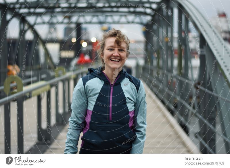SPORTLICH - LACHEN - HAFEN Frau 30 Jahre alt blond Locken lachen sportlich Erwachsene Fröhlichkeit Brücke Brückengeländer Hafen Hamburg trainingsjacke
