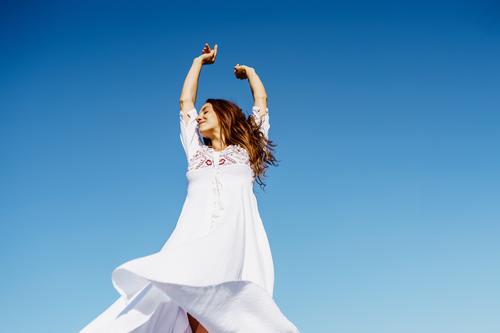 Junge Frau hebt ihre Arme in einem schönen weißen Kleid gegen einen blauen Himmel Mode Mädchen winken offen Waffen Behaarung copyspace Erweiterungen Frisur