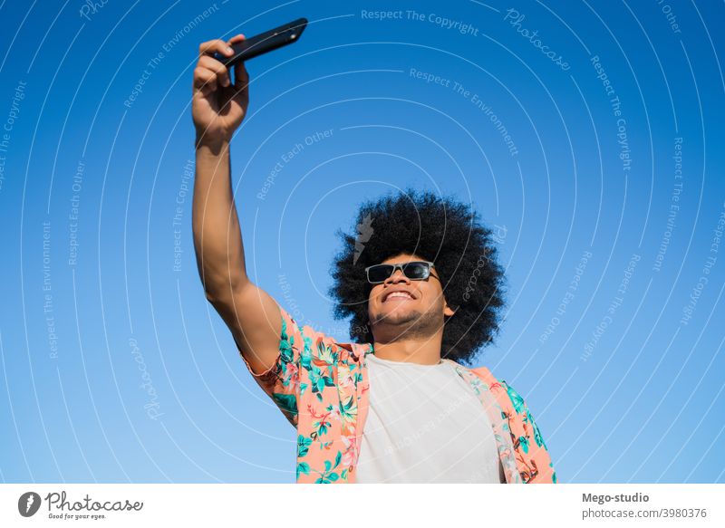 Latino-Mann nimmt ein Selfie mit Telefon im Freien. Latein Mobile urban Tasche Männer reisen Lächeln Konzept Emotion Gerät benutzend Sonnenbrille Sommer