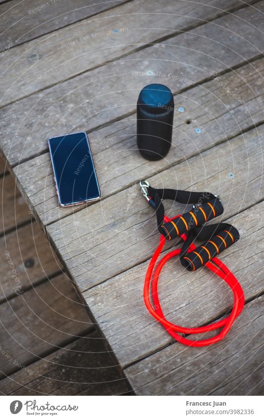 Hohe Winkelaufnahme eines Übungsseils, eines Smartphones und eines Lautsprechers hoch vertikal schwarz rot Holz hölzern Tisch Musik Mobile Telefon Anzeige