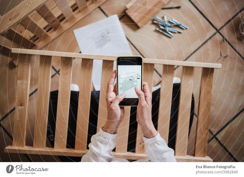 junge Frau beim Zusammenbau von Möbeln zu Hause lesen Anweisungen auf dem Handy. DIY-Konzept es selbst machen heimwärts Technik & Technologie Internet