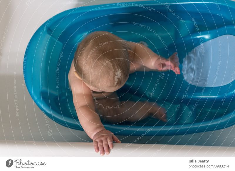 7 Monate altes Baby sitzt aufrecht in blauer Babybadewanne; Hand greift an den Wannenrand Bad Badezeit Sauberkeit Erreichen packen sitzend Säugling Kind