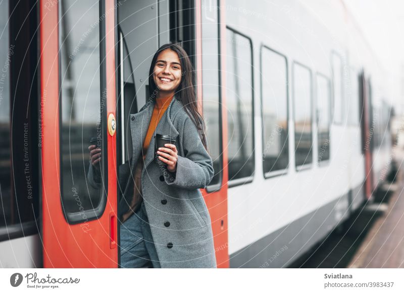 Fröhliches Mädchen steigt am Bahnhof mit Kaffee in der Hand in den Zug ein. Verkehr jung Frau schön Eisenbahn Passagier U-Bahn Lächeln Öffentlich Station Warten