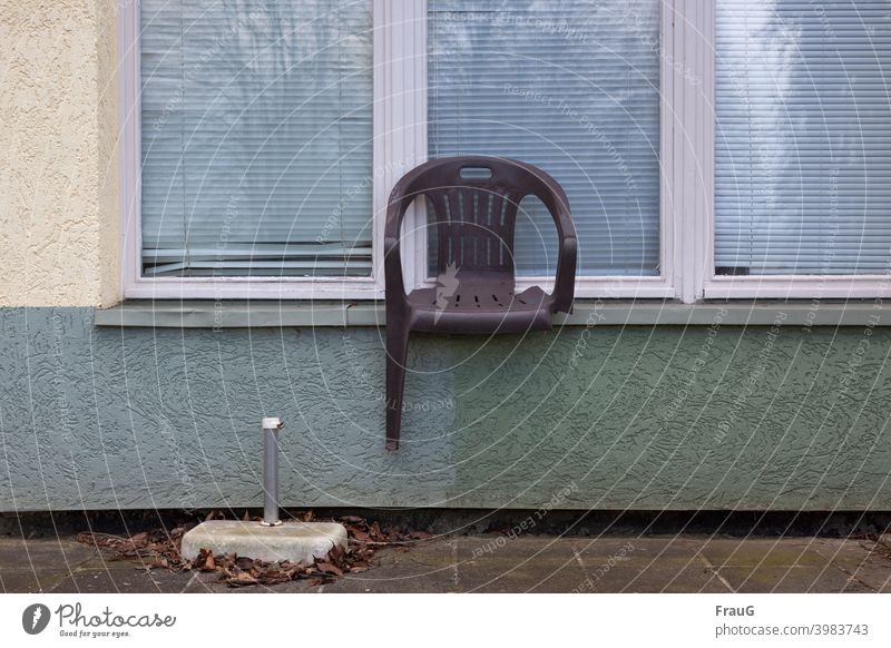 ein kaputter Stuhl auf der Fensterbank Haus Putzfassade Fassade Jalousien Spiegelung Gartenstuhl Stapelstuhl Kunststoff einbeinig alt Sonnenschirm-Ständer Laub