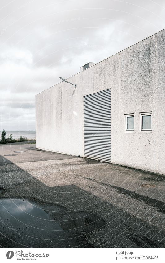 Weiße Fassade einer Lagerhalle mit geschlossenem Rolltor Industrieanlage Gebäude Wand weiß grau Perspektive kühl monochrom gedeckte Farben Hafen Kühlhaus