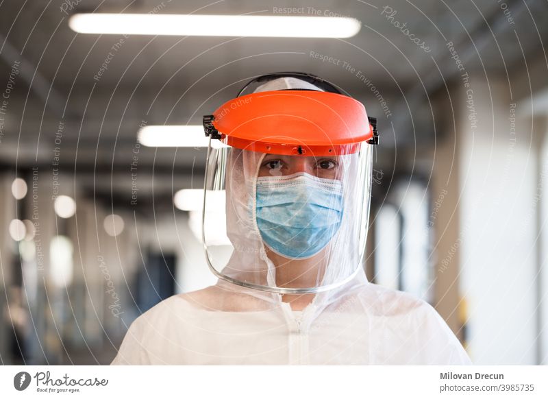 Porträt einer weiblichen Rettungssanitäterin mit persönlicher Schutzausrüstung, Gesichtsmaske und Gesichtsschild, stehend in einem Krankenhausflur oder -korridor