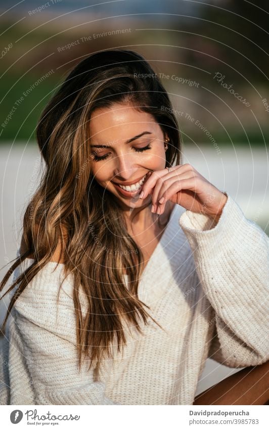 Glückliche junge Frau in modischem Pullover Lächeln ruhen Hof Stil Gesicht berühren Augen geschlossen Angebot Vorschein lange Haare gestrickt weich Freude