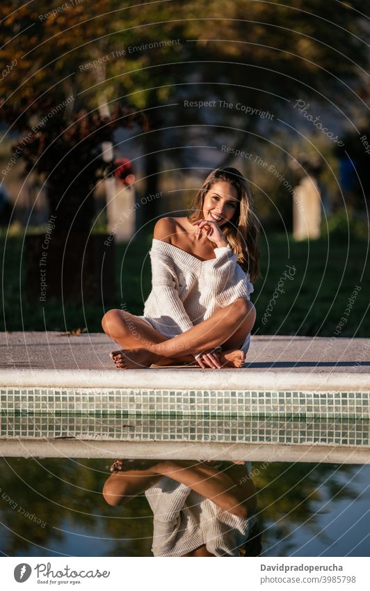 Crop Frau ruht in der Nähe von Pool ruhen Reflexion & Spiegelung Wasser Lächeln Glück Hof tagsüber Windstille Beine gekreuzt Barfuß Sommer sitzen