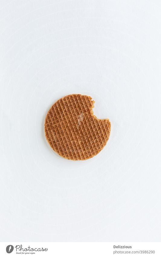 Eine einzelne holländische Stroopwafel (Sirup- oder Karamellwaffel) mit einem Bissen daraus auf weißem Hintergrund backen Biskuit braun Haufen Butter kreisen