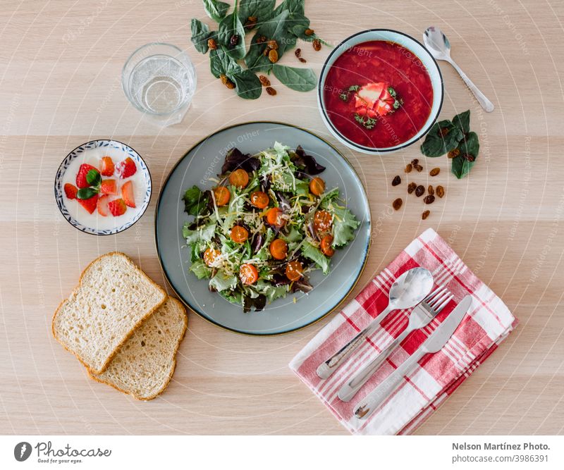 Die Vogelperspektive einer gesunden Mahlzeit. Blattsalat mit Kirschtomaten, zwei Stücke Brot, Joghurt mit Erdbeeren und eine typisch russische Suppe namens Borscht.