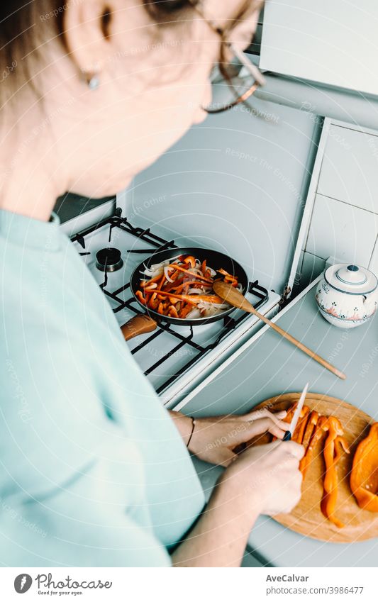 Eine Frau Schneiden einige Pfeffer über eine hölzerne runde Platte mit einem Messer beim Kochen mit der Pfanne in der Küche horizontal Arbeitsplatz Desktop