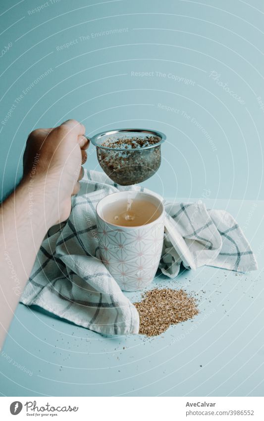 Eine Hand ergreift einen Tee-Destilliergerät über eine Tasse Tee über einen pastellblauen Hintergrund Farben konzeptionell Heilung horizontal entspannend