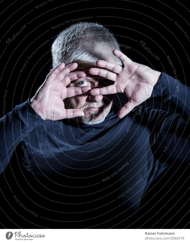 Porträt von einem Mann, der sich mit seinen Händen vor einem grellen Licht schützt. Schutz Mensch Schatten Hand dunkel Angst Panik Finger Arme Mund bedrohlich