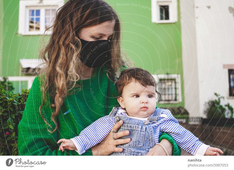 Bild in Grüntönen einer jungen alleinerziehenden Mutter mit ihrem Baby während der Covid-Pandemie COVID Coronavirus Familie Mutterschaft Mama Mundschutz