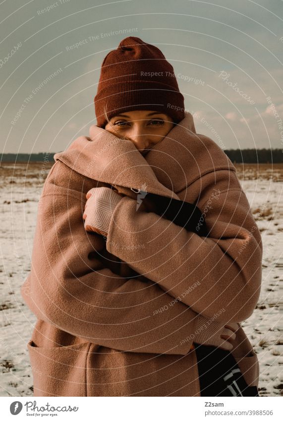 Portrait einer modisch gekleideten Frau in Winterlandschaft winterwonderland frau junge frau mantel spaziergang schnee sonne licht natur schal mütze lange haare