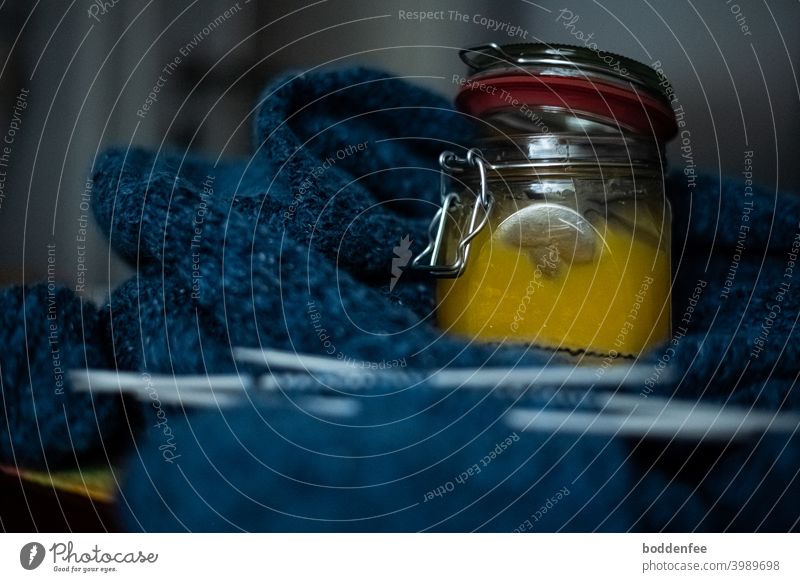 Ein gefülltes Honigglas steht als Nervennahrung auf einer blauen Strickarbeit, fokussiert auf das Glas mit unscharfem Vorder- und Hintergrund stricken