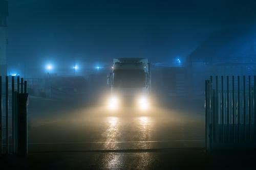 Lkw verlässt eine Fabrik bei Nacht an einem sehr nebligen Tag mit schlechter Sicht. Lastwagen Nebel Lichter Dunkelheit Vorderansicht Gate Transport Verkehr groß