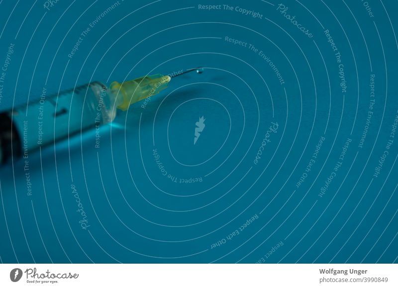Eine Spritze mit Flüssigkeitstropfen auf blauem Hintergrund vereinzelt Korona Nahaufnahme Stoß Impfung kalt Grippe Gesundheit Pflege Medikament Medizin Jena