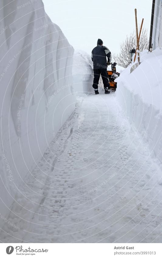 Bei starkem Schneefall räumt ein Mann in Bayern mit einer Schneefräse den Gehweg frei schneeräumen schneefräsen mann schneien winter räumdienst schneeschaufeln