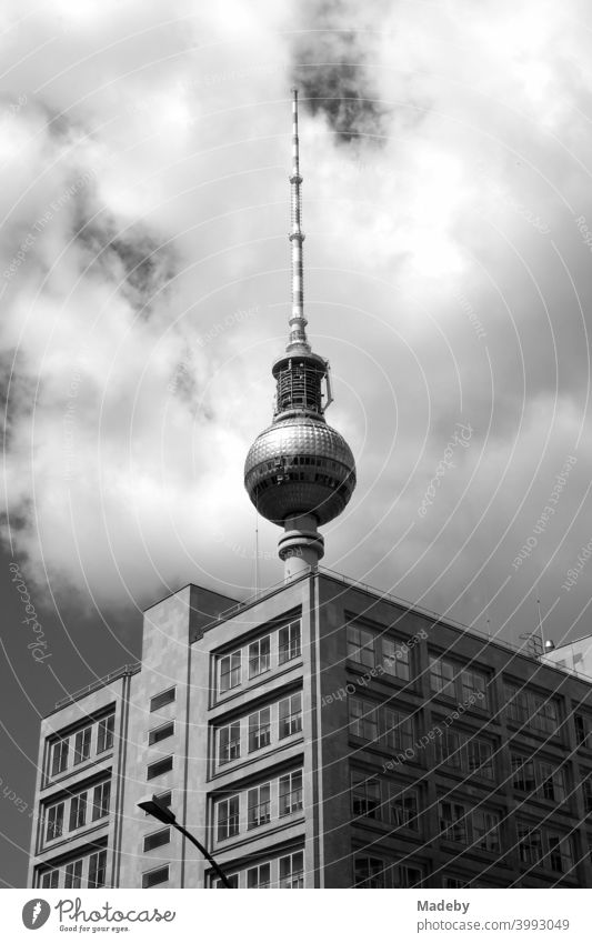 Der Berliner Fernsehturm hinter einem kubischen Bürogebäude mit Wolken bei Sonnenschein am Alexanderplatz in der Hauptstadt Berlin, fotografiert in klassischem Schwarzweiß