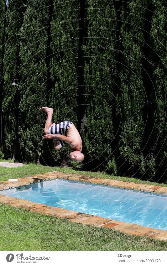 Ein Mann springt mit einem Purzelbaum in den Pool. Springt kopfüber ins Wasser. fallend Schwimmsport männlich Urlaub Sonnenbrille ohne Hemd kahl Badeanzug