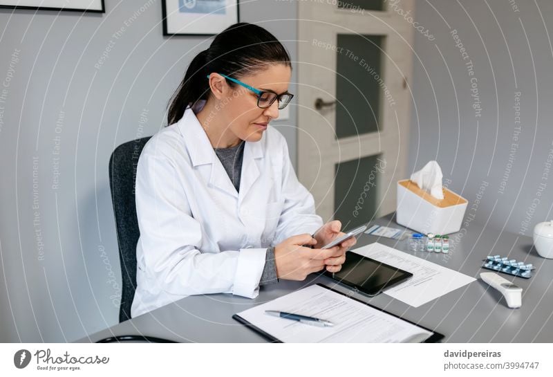 Ärztin benutzt Handy während der Arbeit Arzt Frau arbeiten benutzend Arztpraxis Lächeln Texten professionell plaudernd medizinisch Büro Medizin Klinik Beruf