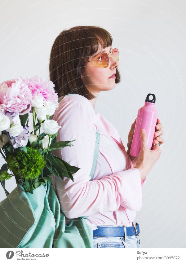 Junge Frau in Rosa mit Rucksack und wiederverwendbarer Flasche keine Verschwendung Frühling Blumen Sommer rosa Sonnenbrille Wasser Thermoskanne authentisch