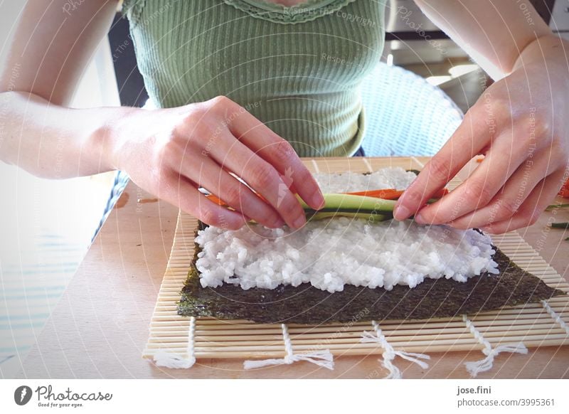 Hände einer Frau, Sushi selbst zubereitend Oberkörper Essen zubereitung Küche Reis Lachs Japanisch Asiatische Küche traditionell Wasabi Ingwer Holztisch