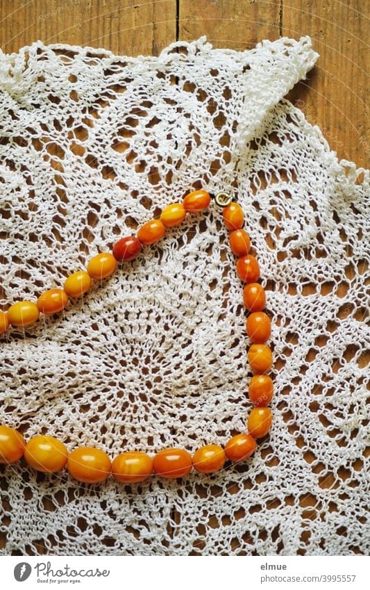bernsteinfarbene Perlenkette auf einem handgehäkelten Deckchen / Schmuck / Halskette Kette handgefertigt Holztisch Handarbeit Modeschmuck dekorativ häkeln