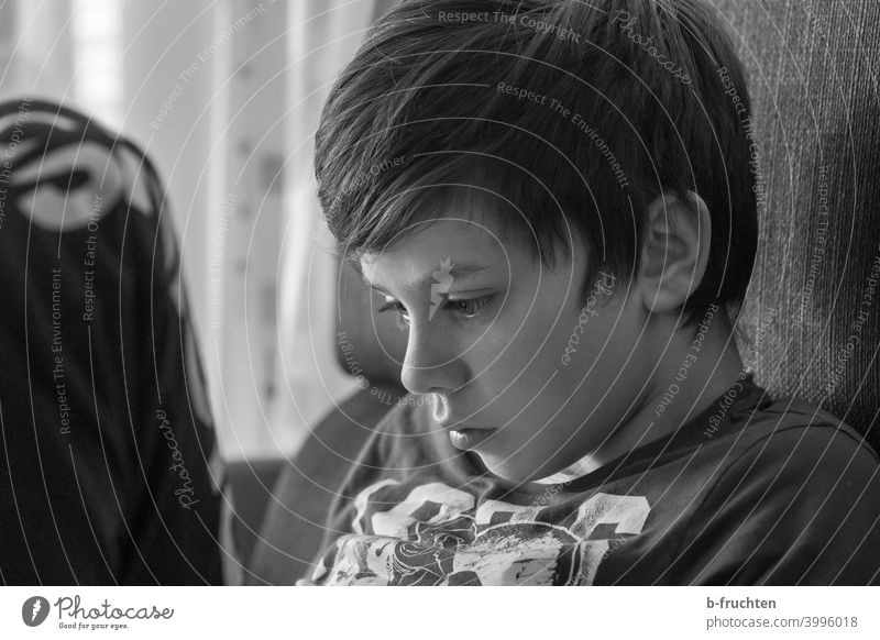 Kind sitzt auf der Couch mit Blick auf das Smartphone Junge Porträt Kindheit Gesicht Auge Haare & Frisuren Spielen Sofa sitzen bequem Schwarzweißfoto Kopf Ruhe