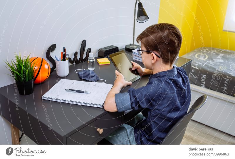 Teenager macht Hausaufgaben mit einem Tablet Tablette Schule zu Hause Coronavirus Maske auf dem Schreibtisch Flasche für Handdesinfektionsmittel Jugendzimmer