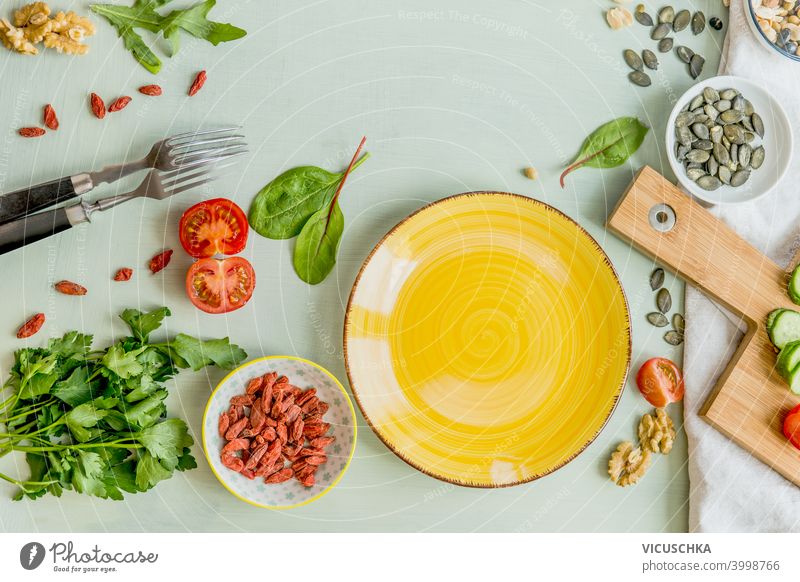 Leerer gelber Teller auf grünem Tisch mit Gabeln und gesunden Salatzutaten. Ansicht von oben. Gesundes Mittagessen Vorbereitung blanko Gesundheit Salatbeilage