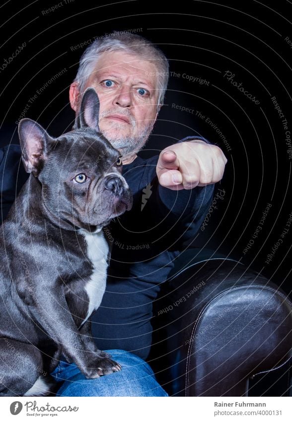 Beste Freunde, Hund und Mensch. Ein Mann zeigt mit dem Finger und passt auf, die Französische Bulldogge wirkt unbeteiligt. Der Hintergrund ist schwarz.