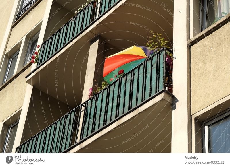 Farbenfroher Sonnenschirm auf dem Balkon eines naturfarbenen Mietshaus im Stil der Nachkriegszeit im Sommer bei Sonnenschein in Frankfurt am Main in Hessen