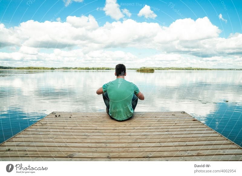 junger Mann sitzt auf einem Steg in der Natur und genießt die absolute Ruhe See ruhe sitzen genießen abstand Erholung entspannung abschalten