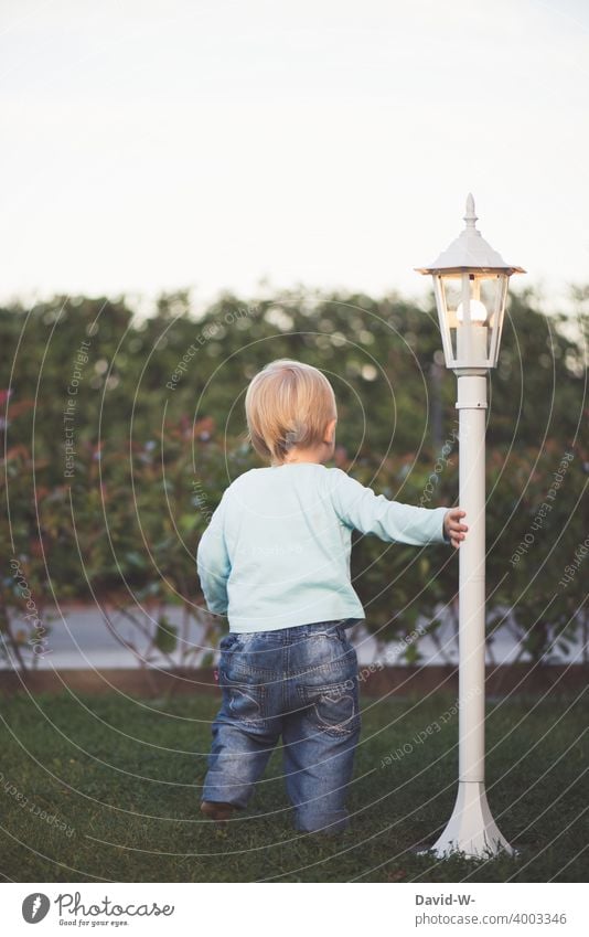 Kleinkind steht neugierig im Garten und hält sich an einer Lampe fest Kind Frühling Laterne interessiert erkunden Kindheit niedlich