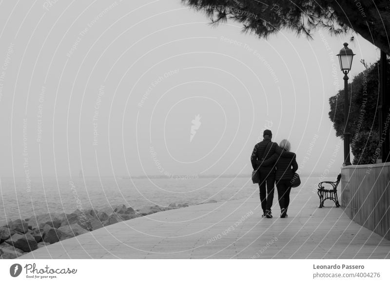 Ein Paar geht an einem nebligen Tag am Wasser entlang - Grado, Italien MEER Pier Nebel Winter schwarz auf weiß Schwarz-Weiß-Fotografie Schwarz-Weiß-Landschaft