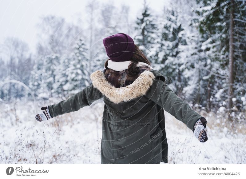 Junges Mädchen, Frau geht in schönen Winterwald unter Bäumen, Tannen, mit Schnee bedeckt. Magnificent Natur und Ansichten. Modisches Bild, Kleidung, Parka, Hut, Handschuhe, Blue Jeans
