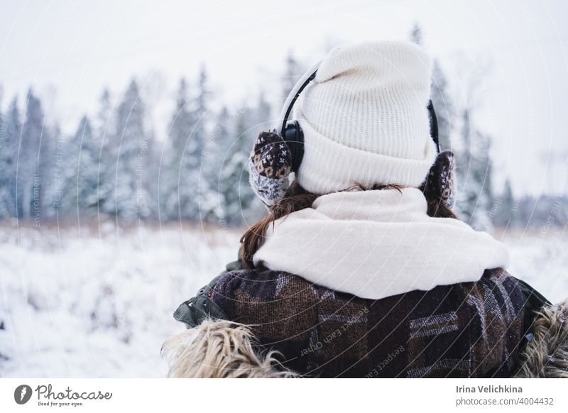 Junges Mädchen, Frau in gestrickten Fäustlingen hören Musik auf Kopfhörer. Walking in schönen Winterwald unter Bäumen, Tannen, mit Schnee bedeckt. Prächtige Natur. Modisches Bild, Kleidung, Parka, Hut