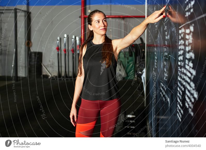 Frau, die auf Trainingspläne zeigt. Crossfit Funktionstraining Übung Gesundheit Sport Fitnessstudio Gewicht Gebäude bügeln Hanteln Muskel Trainerin Aktivität