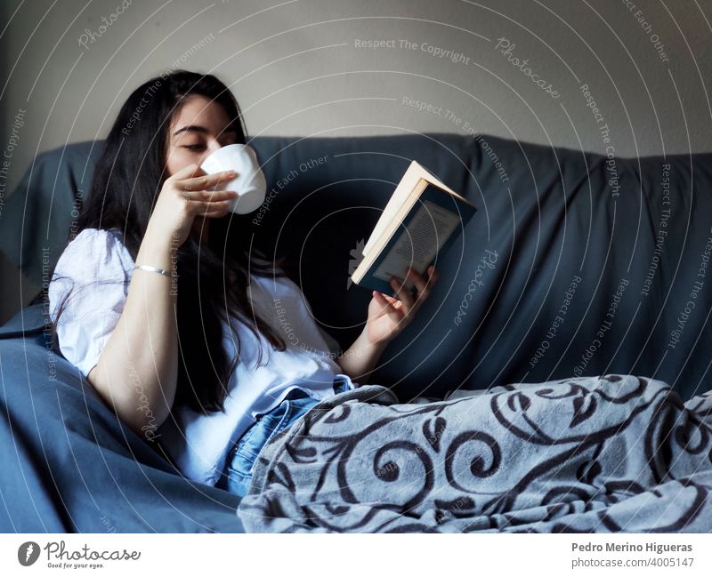 Frau trinkt aus einer Tasse Kaffee und liest ein Buch sich[Akk] entspannen warm weich niedlich ruhen schön Glück jung lebend Innenbereich Erholung Fenster