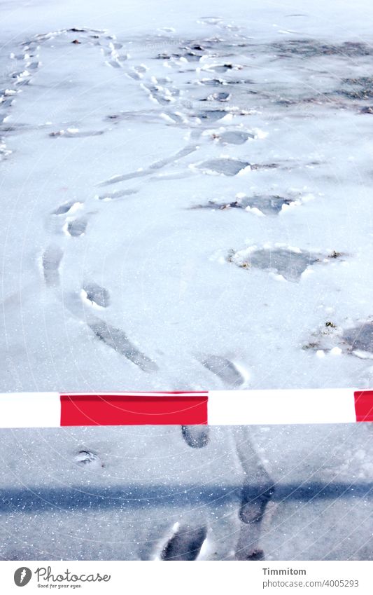 Eine Absperrung und Fußspuren im Schneematsch Absperrband rot weiß Schatten Winter kalt Übertretungen Spuren Menschenleer Flatterband Außenaufnahme