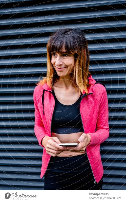 Sportlerin mit Mobiltelefon Frau Athlet Lächeln Gitterrost-Hintergrund Mobile zur Seite schauend posierend Porträt Taille hoch Fitness Smartphone Gesundheit